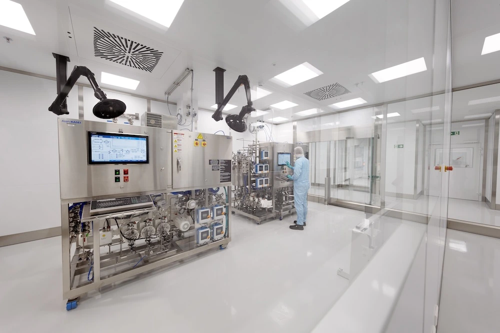 A scientist in full cleanroom clothing operates advanced bioprocessing equipment in a sterile, state-of-the-art laboratory at Axolabs CDMO site in Berlin.