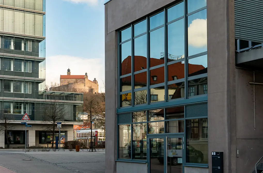 Modern office buildings with large glass windows reflecting surrounding historic architecture and a castle on a hill in the background.