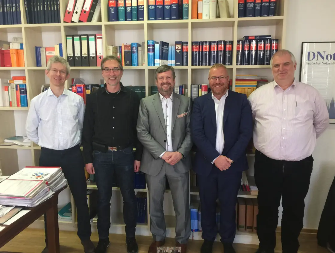 Five men stand smiling in front of a large bookshelf filled with legal and technical books and folders in an office setting.